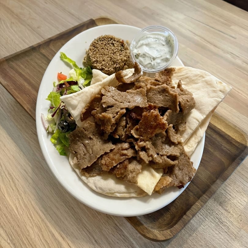 Doner kebab plate with sliced meat, pita bread, rice, salad, and a side of tzatziki sauce.