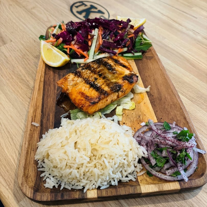 Grilled salmon with rice, red cabbage salad, and red onion salad on a wooden board.